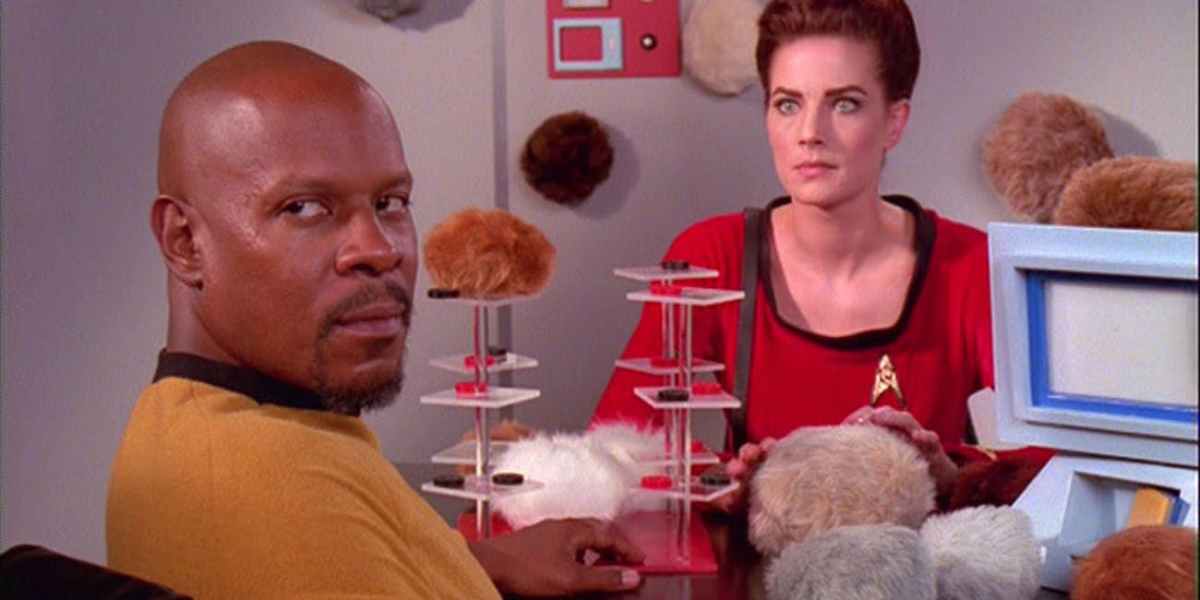 Commander Sisko and Jadzia Dax look off screen while handling a pile of fluffy balls in Star Trek